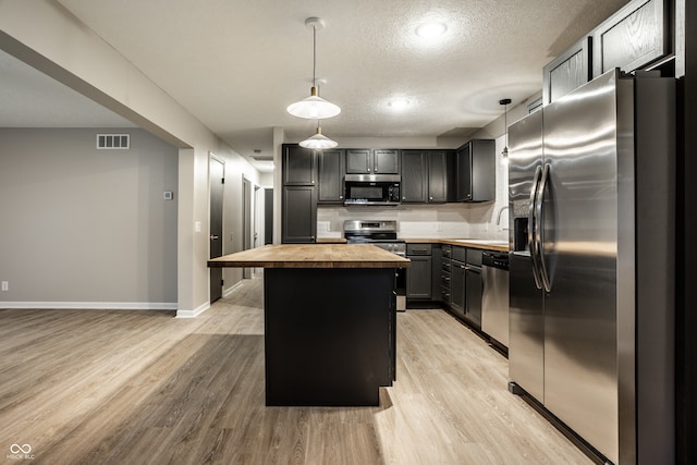 kitchen with a kitchen island, appliances with stainless steel finishes, butcher block countertops, hanging light fixtures, and light hardwood / wood-style flooring