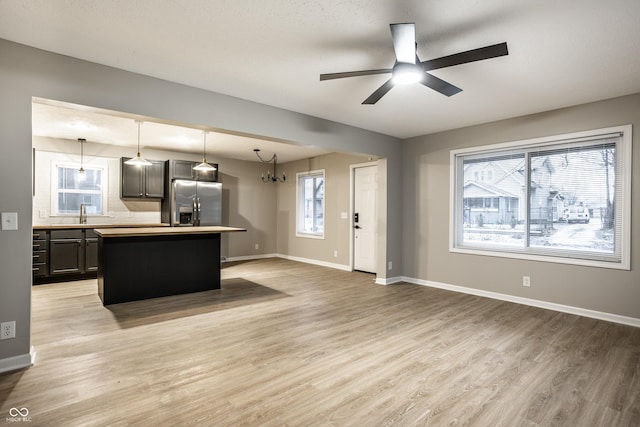 kitchen with ceiling fan, stainless steel refrigerator with ice dispenser, a kitchen island, decorative light fixtures, and light wood-type flooring