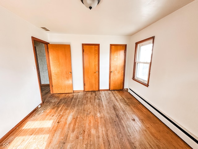 unfurnished bedroom featuring a baseboard heating unit, two closets, and light wood-type flooring