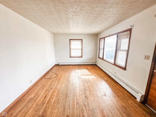 empty room featuring hardwood / wood-style flooring, a baseboard radiator, and a textured ceiling