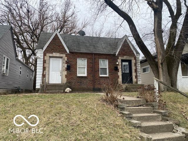 view of front of house featuring a shingled roof, entry steps, brick siding, and a front lawn