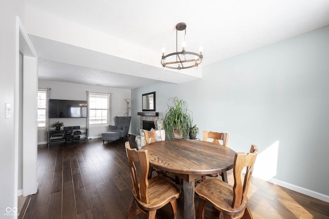 dining area with a chandelier, a stone fireplace, dark wood-type flooring, and baseboards