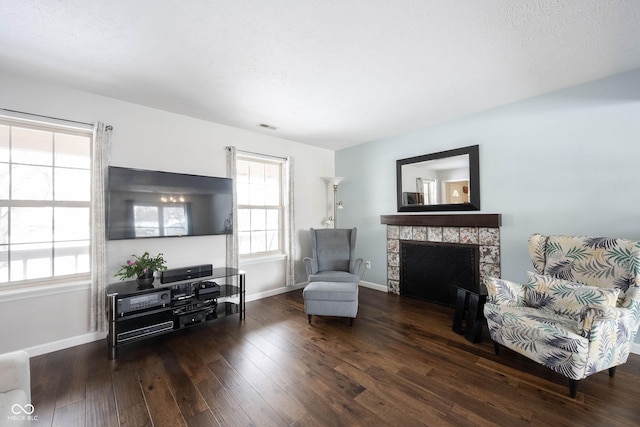 living area with visible vents, baseboards, dark wood-type flooring, a textured ceiling, and a stone fireplace