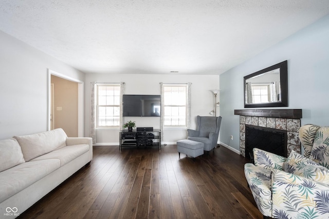 living room featuring a textured ceiling, a fireplace, baseboards, and dark wood-style flooring