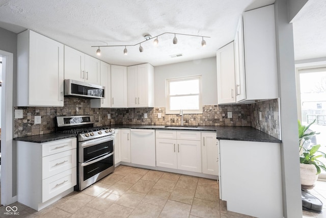 kitchen with stainless steel appliances, a sink, visible vents, white cabinets, and dark countertops