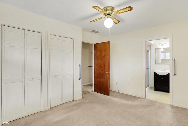 unfurnished bedroom with two closets, sink, light colored carpet, ceiling fan, and ensuite bath