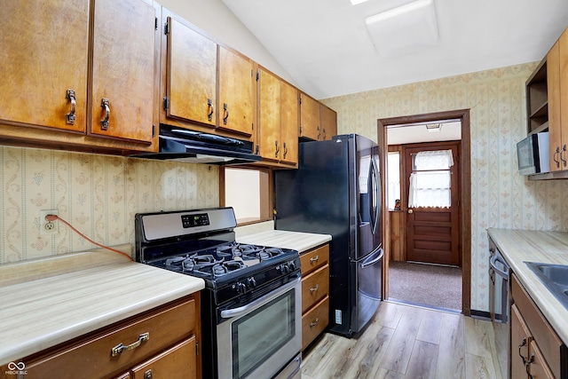 kitchen with stainless steel appliances, vaulted ceiling, and light hardwood / wood-style floors