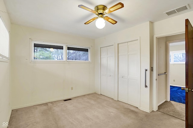 unfurnished bedroom featuring multiple closets, ceiling fan, light colored carpet, and multiple windows