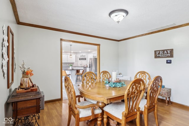 dining space featuring crown molding, a textured ceiling, and light wood-type flooring