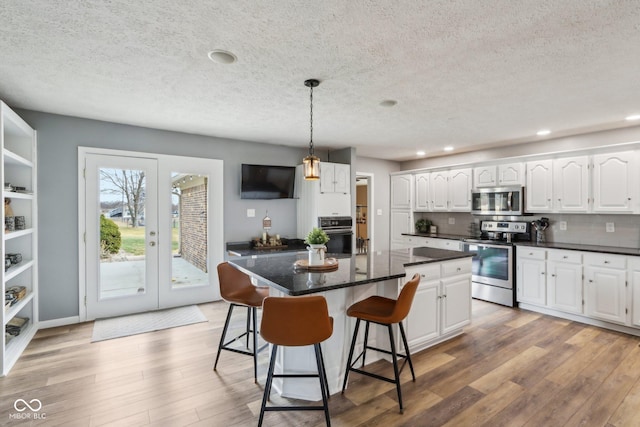 kitchen with decorative light fixtures, white cabinetry, a center island, stainless steel appliances, and light wood-type flooring