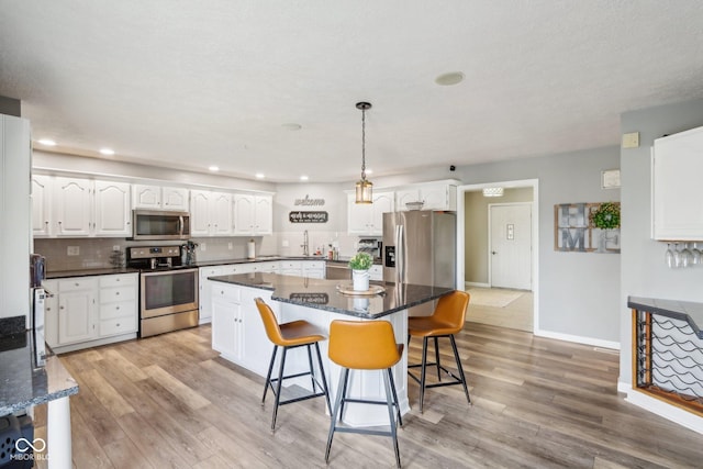 kitchen featuring white cabinetry, hanging light fixtures, a kitchen island, and appliances with stainless steel finishes