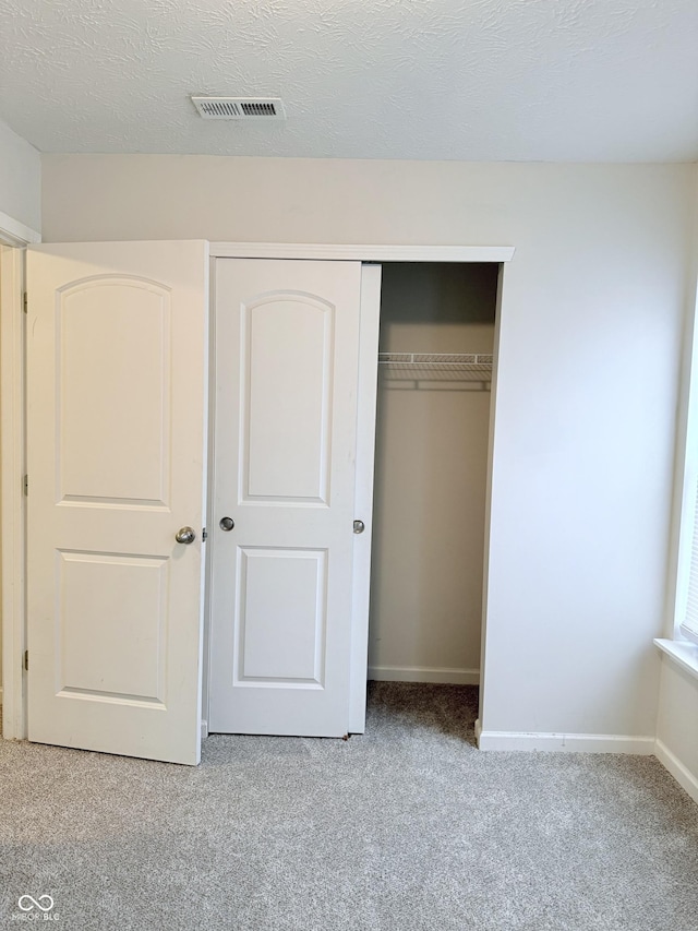 unfurnished bedroom featuring light colored carpet, a closet, and a textured ceiling