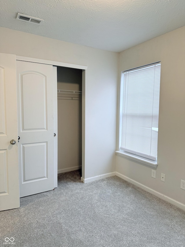 unfurnished bedroom featuring light carpet, a textured ceiling, and a closet