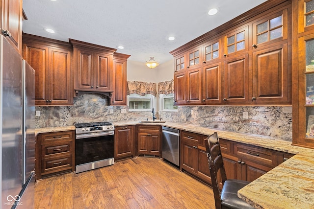 kitchen with sink, hardwood / wood-style floors, stainless steel appliances, tasteful backsplash, and light stone countertops