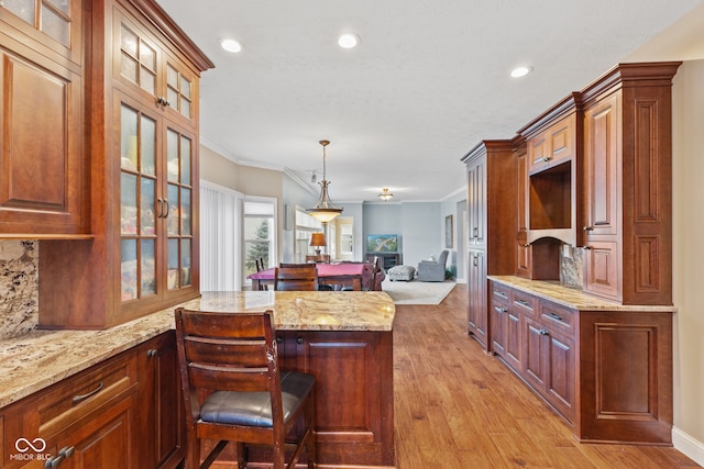 kitchen with a breakfast bar, pendant lighting, light hardwood / wood-style floors, crown molding, and light stone countertops