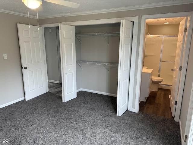 unfurnished bedroom featuring ornamental molding, ensuite bathroom, dark carpet, and a closet