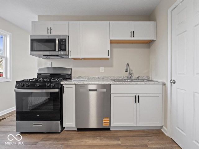 kitchen with sink, appliances with stainless steel finishes, white cabinetry, wood-type flooring, and light stone countertops