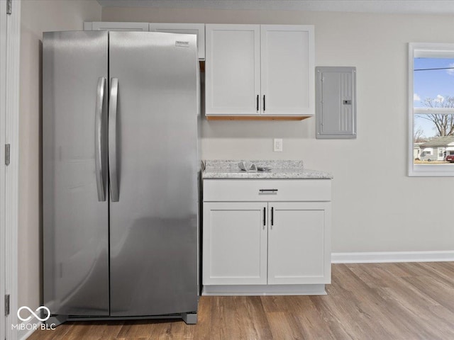 kitchen featuring stainless steel refrigerator, white cabinetry, electric panel, and light hardwood / wood-style flooring