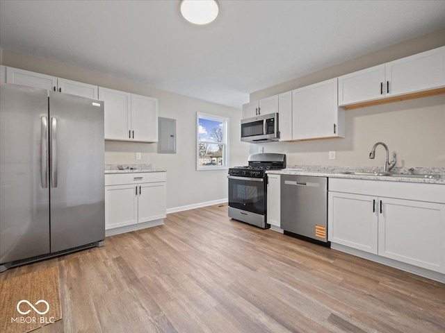 kitchen featuring sink, white cabinetry, stainless steel appliances, light stone counters, and light hardwood / wood-style floors