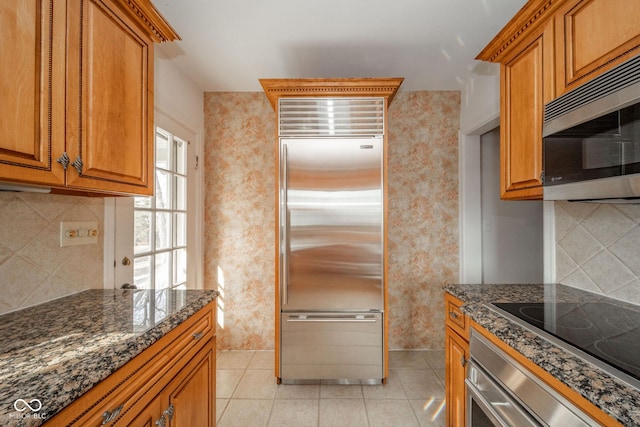 kitchen with tasteful backsplash, light tile patterned floors, stainless steel appliances, and dark stone counters