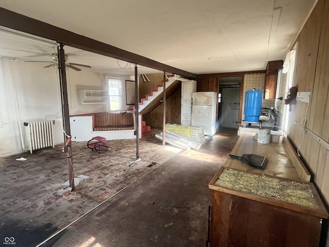 basement with white refrigerator, ceiling fan, radiator, and a wall unit AC