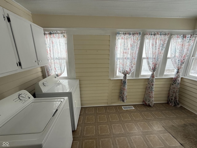 clothes washing area featuring separate washer and dryer, wood walls, and cabinets