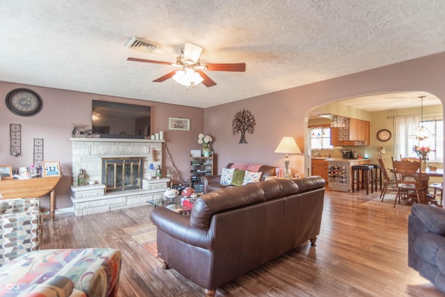 living room with ceiling fan, a fireplace, hardwood / wood-style floors, and a textured ceiling