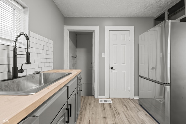 kitchen featuring butcher block countertops, sink, light hardwood / wood-style flooring, stainless steel refrigerator, and backsplash