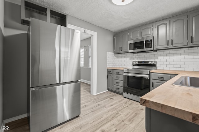 kitchen featuring appliances with stainless steel finishes, gray cabinetry, wooden counters, and light wood-type flooring