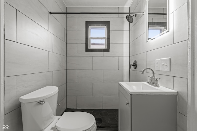 bathroom with vanity, tiled shower, tile walls, and toilet