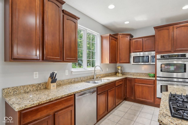 kitchen with appliances with stainless steel finishes, light stone countertops, sink, and light tile patterned floors