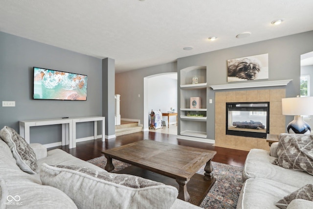 living room with a tiled fireplace, wood-type flooring, and built in features