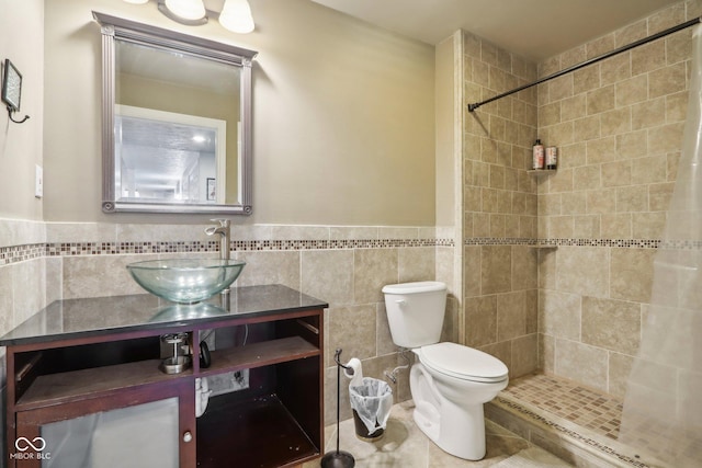 bathroom with tiled shower, vanity, toilet, and tile walls