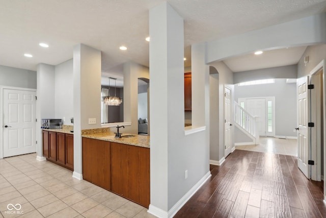 kitchen with pendant lighting, sink, kitchen peninsula, light stone countertops, and light wood-type flooring