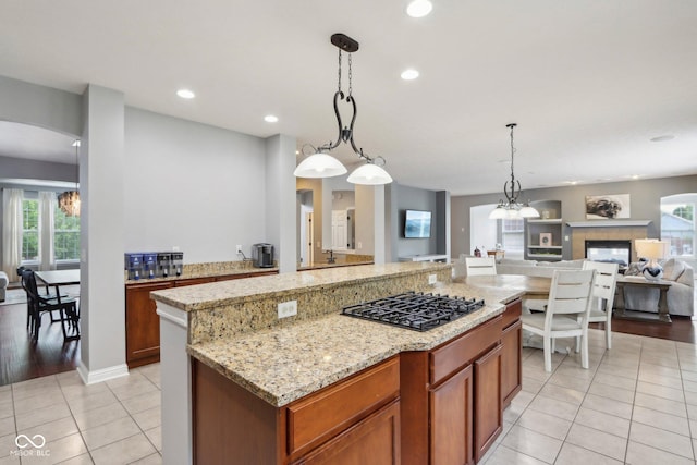 kitchen with a center island, hanging light fixtures, light tile patterned floors, black gas cooktop, and light stone countertops