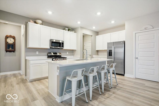 kitchen featuring white cabinetry, sink, stainless steel appliances, a center island with sink, and light wood-type flooring