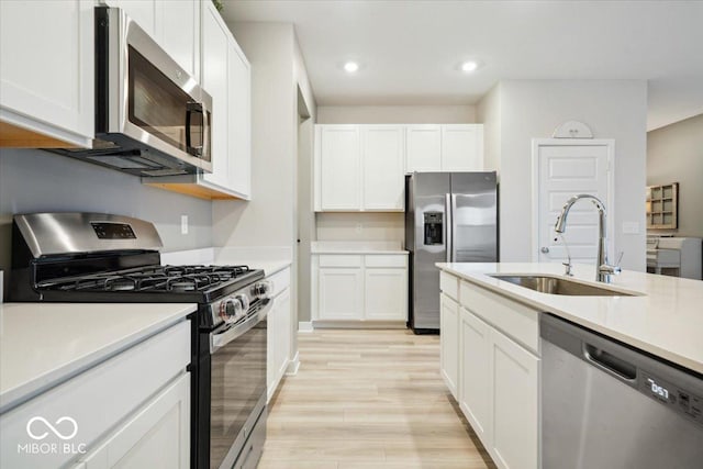 kitchen with appliances with stainless steel finishes, sink, light hardwood / wood-style flooring, and white cabinets