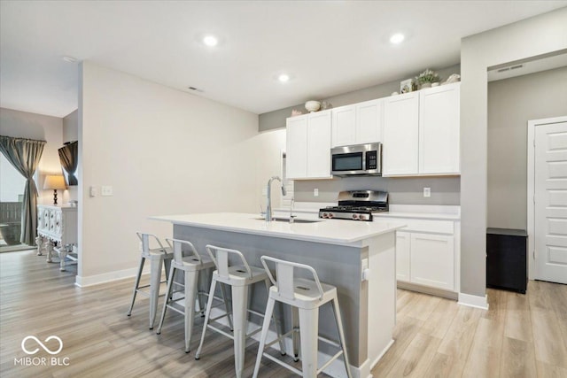 kitchen featuring sink, stainless steel appliances, light hardwood / wood-style floors, white cabinets, and a center island with sink