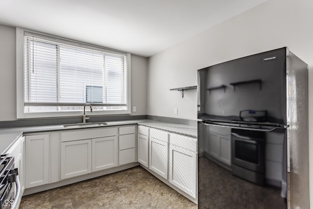 kitchen with white cabinetry, sink, stainless steel gas range oven, and black fridge