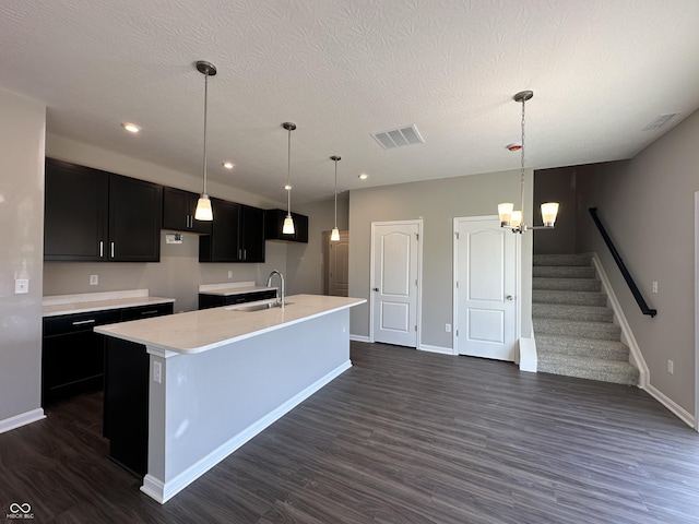 kitchen with a sink, visible vents, dark cabinets, and a center island with sink