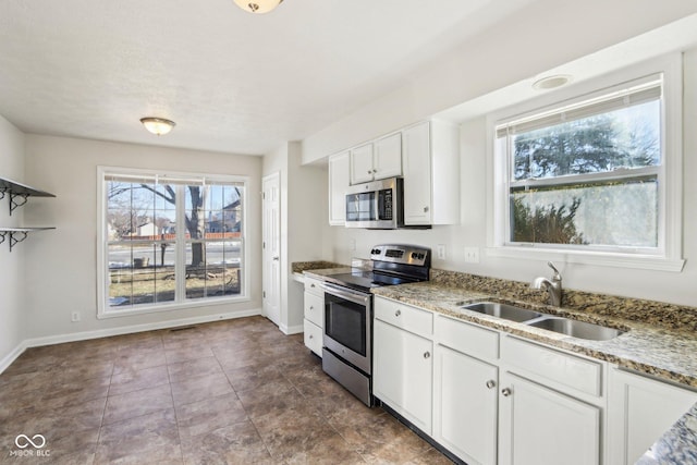 kitchen with appliances with stainless steel finishes, white cabinetry, sink, light stone countertops, and tile patterned floors