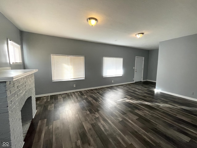 unfurnished living room featuring a brick fireplace and dark hardwood / wood-style floors