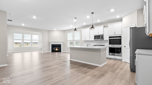 kitchen with white cabinetry, stainless steel appliances, a center island with sink, decorative light fixtures, and light wood-type flooring