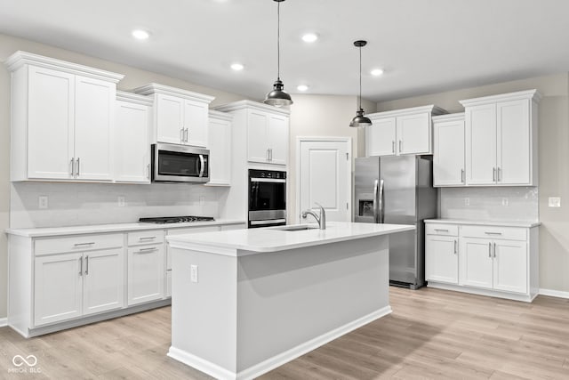 kitchen with appliances with stainless steel finishes, white cabinetry, an island with sink, hanging light fixtures, and light hardwood / wood-style flooring