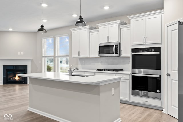 kitchen with stainless steel appliances, white cabinetry, pendant lighting, and an island with sink