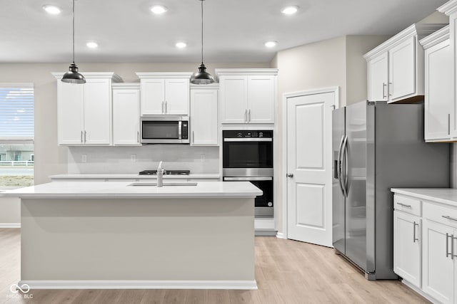 kitchen featuring stainless steel appliances, white cabinetry, hanging light fixtures, and a center island with sink