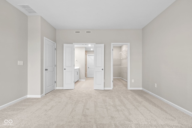 unfurnished bedroom featuring light colored carpet, ensuite bathroom, a spacious closet, and a closet