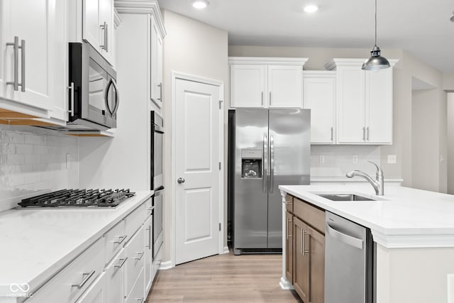 kitchen with appliances with stainless steel finishes, white cabinetry, sink, hanging light fixtures, and a center island with sink