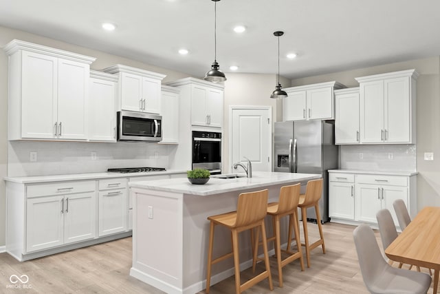 kitchen with appliances with stainless steel finishes, white cabinets, hanging light fixtures, a center island with sink, and light hardwood / wood-style flooring