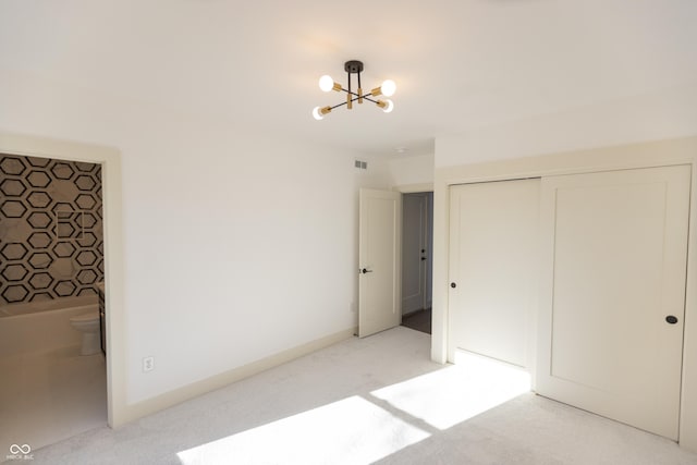 unfurnished bedroom featuring an inviting chandelier, ensuite bath, light colored carpet, and a closet